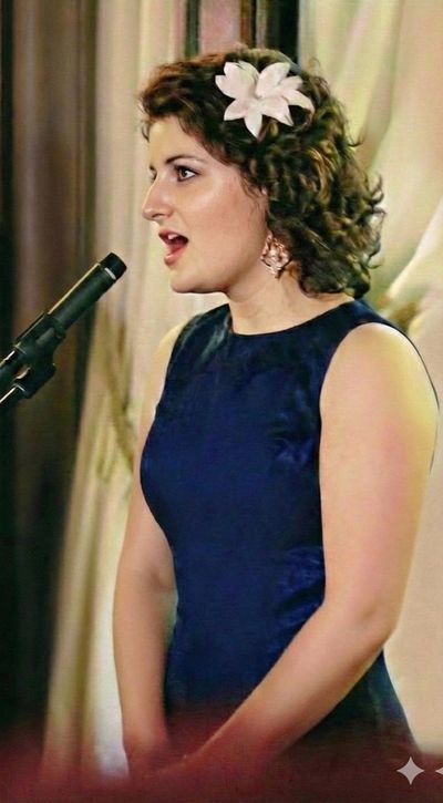 Tess Howell in a blue dress with a flower in her hair, singing into a microphone.